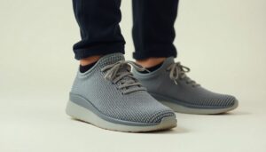 A person wearing dark trousers and light grey Nexus Knit minimalist footwear by Xero Shoes with white soles, standing on a light surface. The shoes feature laces and a textured pattern.